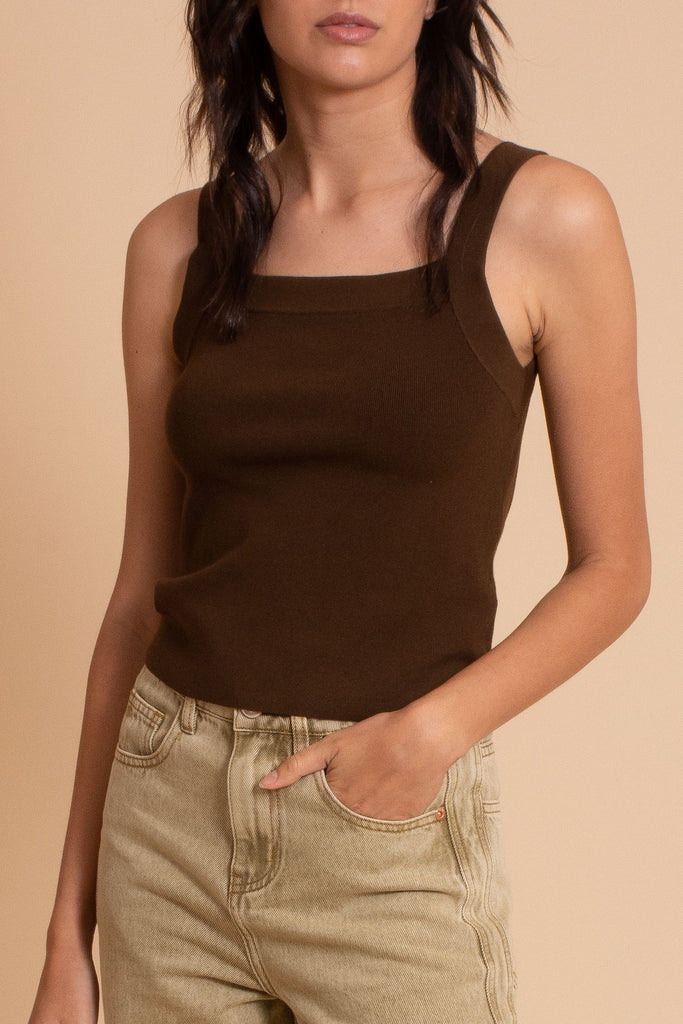 Model with hand in her pocket wearing brown ribbed knit tank top and light grey demin jeans
